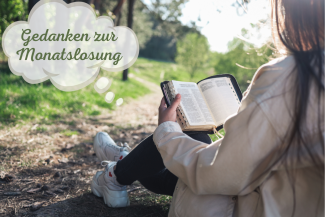 Frau sitzt an Baum gelehnt und liest in der Bibel